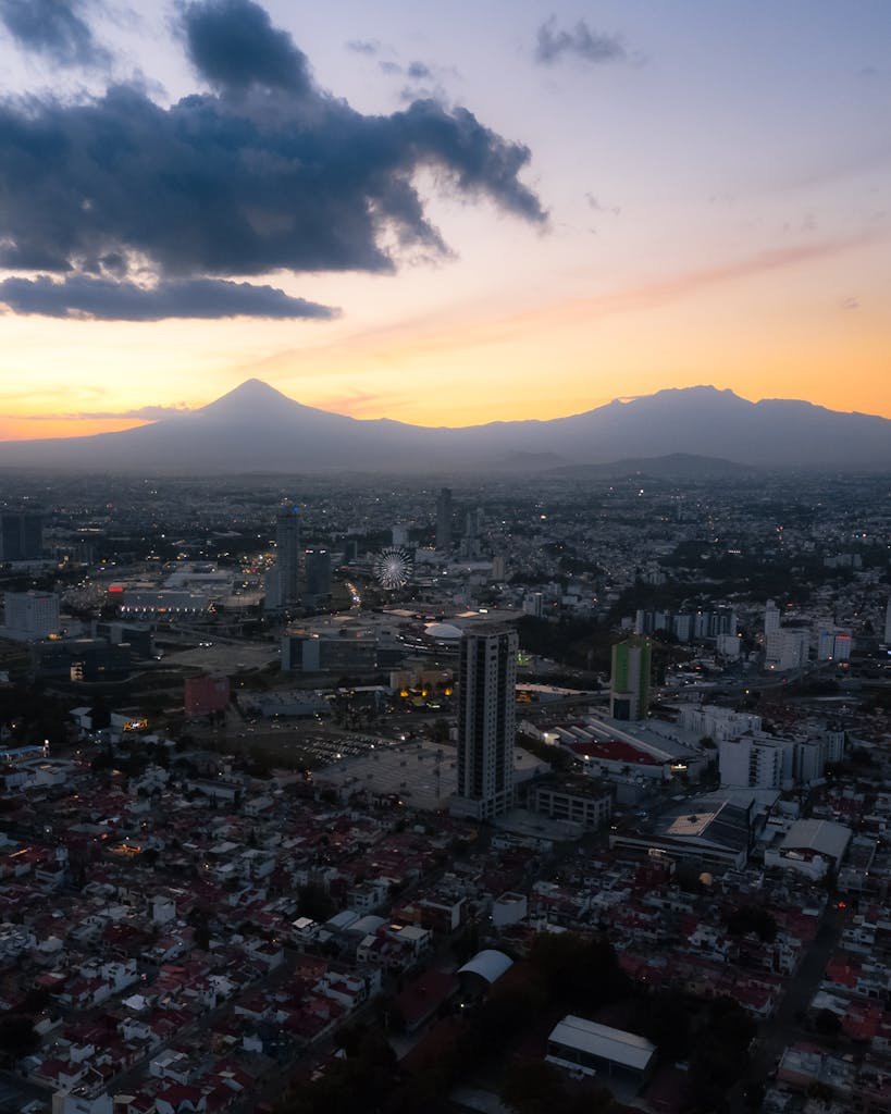 Captivating aerial view of Puebla cityscape at sunset, featuring a silhouetted volcano.